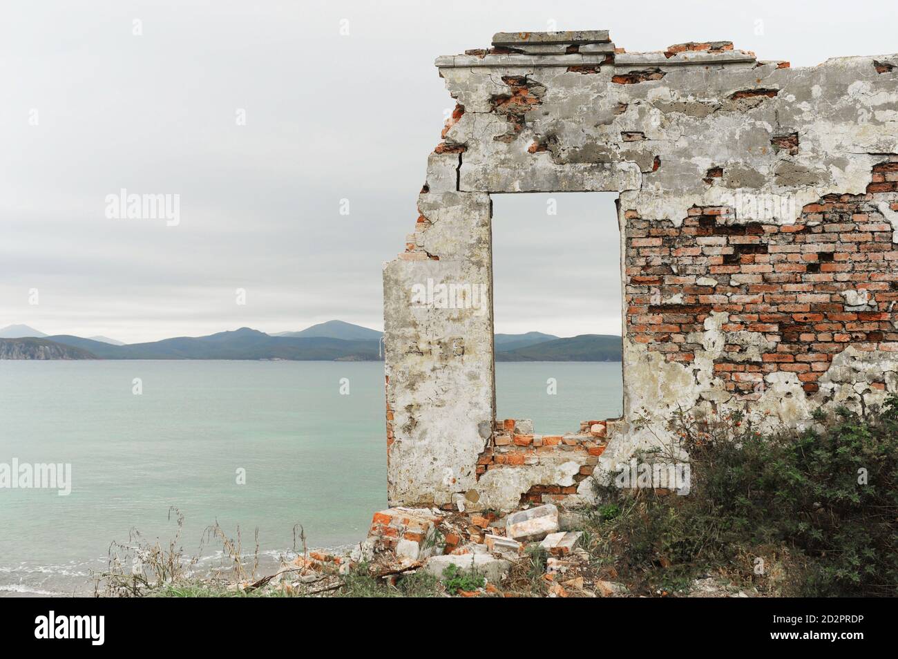 remains of ruined old brick house and window without glass with view of beautiful blue clear sea and mountains, selective focus Stock Photo
