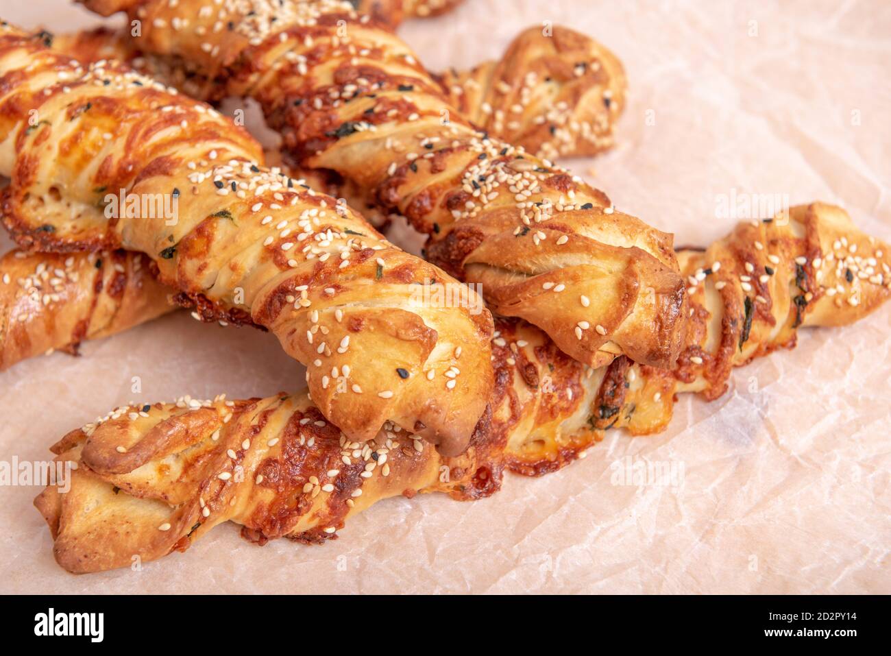 Twisted puff pastry sticks on white paper parchment, wood table Stock Photo