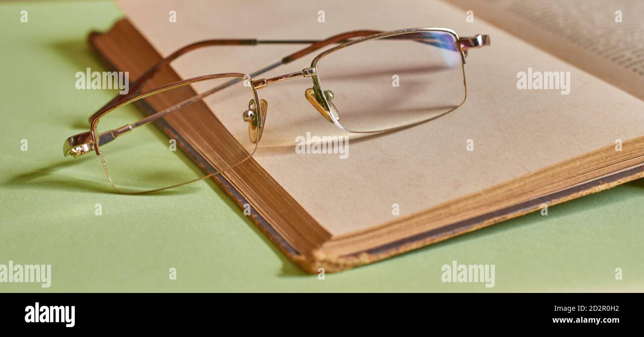 The glasses are lying on an open book on a solid green background Stock Photo