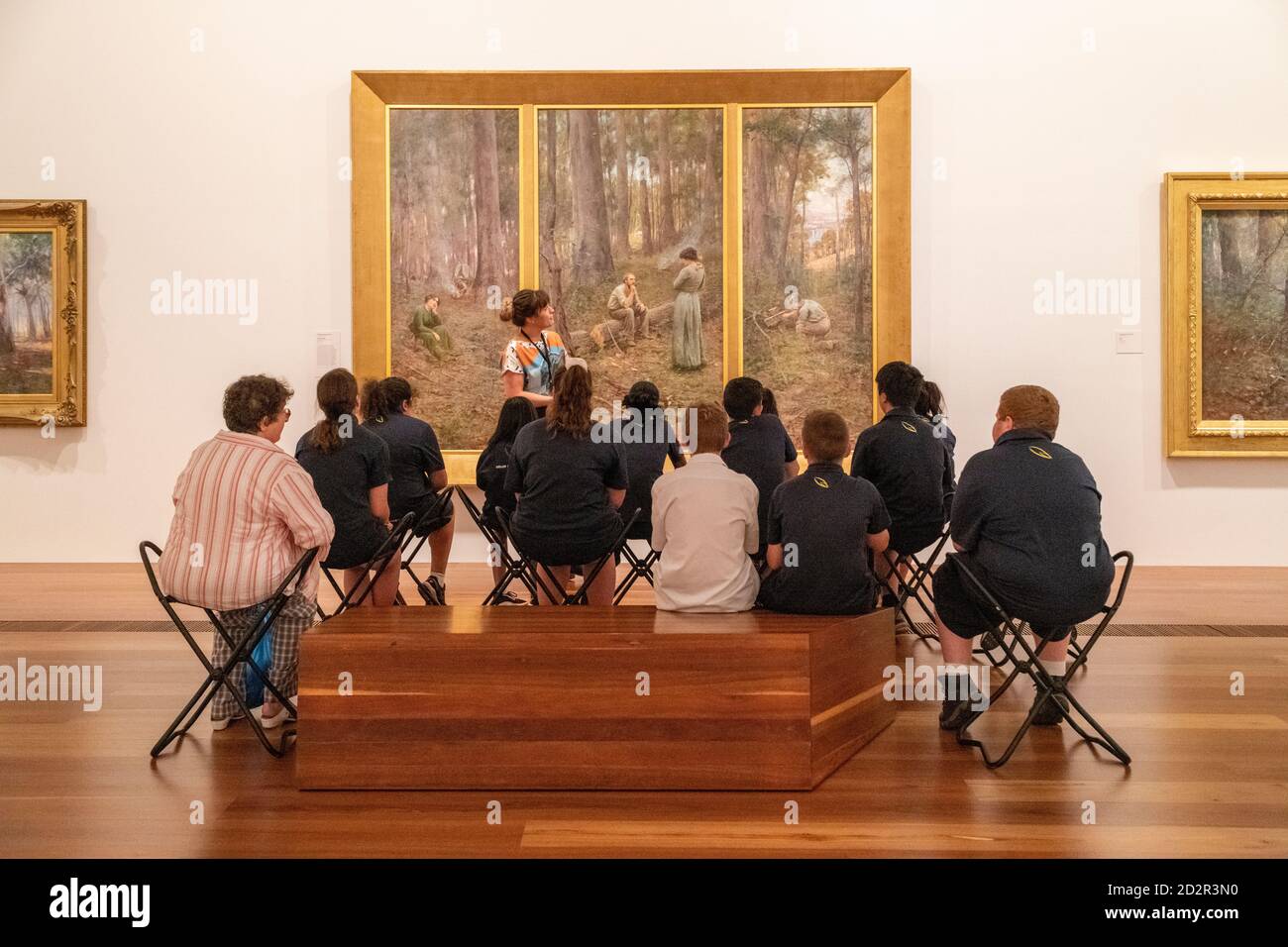 Students listen to a guide discussing a painting in the National Gallery of Victoria. Stock Photo