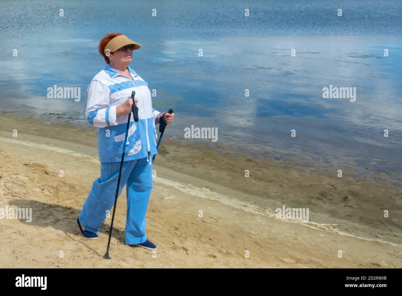 An elderly woman trains in Nordic walking with sticks. Taking care of health and an active lifestyle in old age. Soft focus, blur. Stock Photo