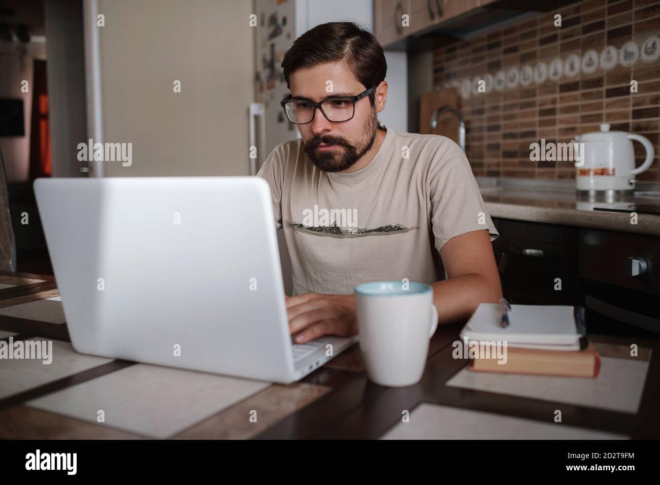 Focused young man wearing glasses using laptop, typing on keyboard, writing email or message, chatting, shopping, successful freelancer working online Stock Photo
