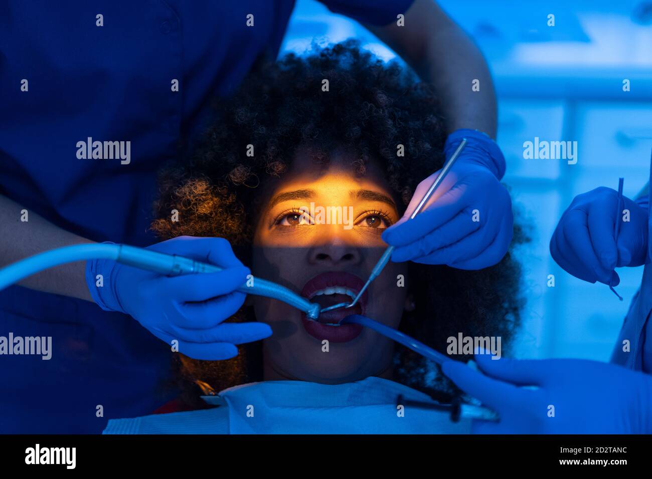 Crop of dentist and assistant using dental suction device on teeth of black Woman in clinic