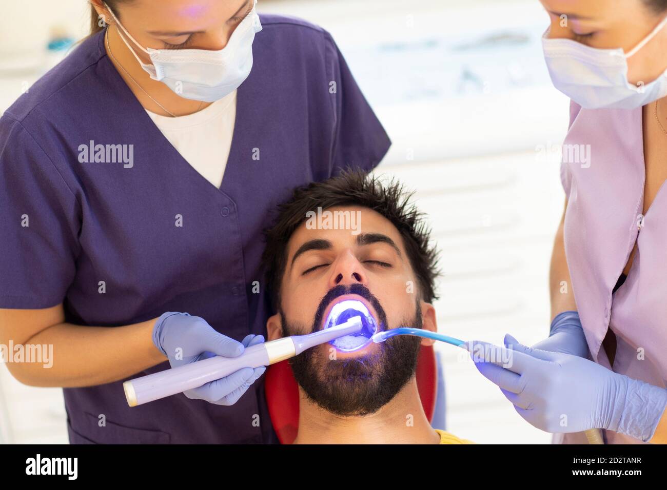 Female dentist and assistant using dental curing light and suction