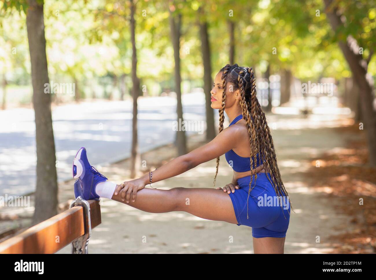 Side view of ethnic female athlete wearing sports bra and shorts stretching  legs and warming up body before training in summer park Stock Photo - Alamy