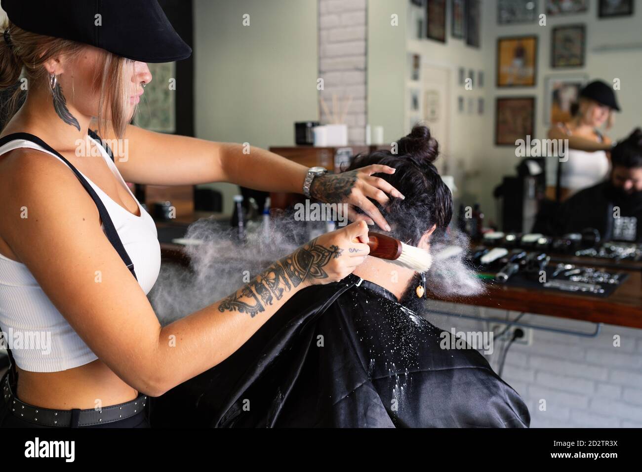 Professional female hipster applying talcum powder on neck of male customer after shaving procedure in modern barbershop Stock Photo