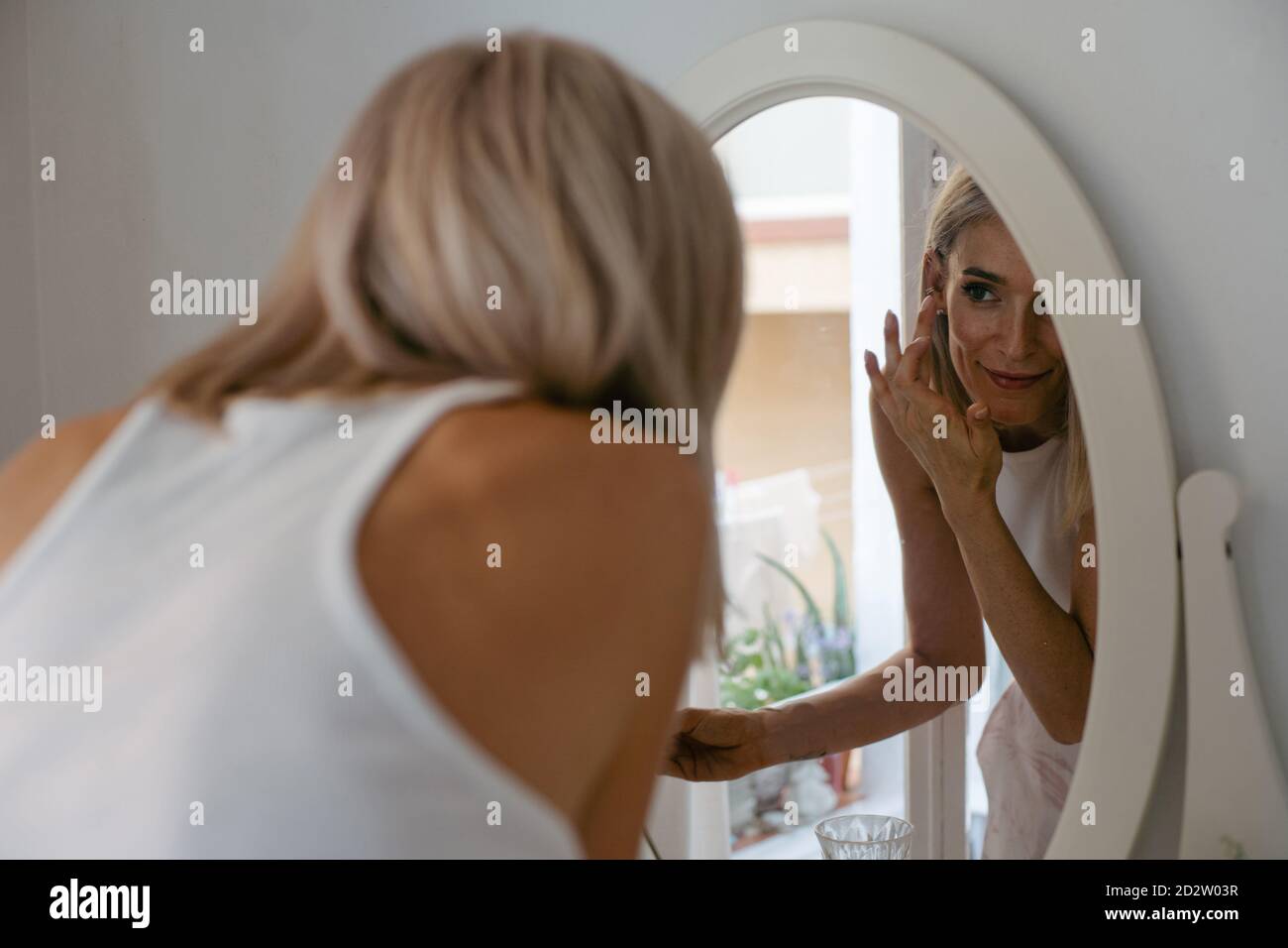 Charming female applying lip pencil and doing makeup at home while reflecting in mirror Stock Photo