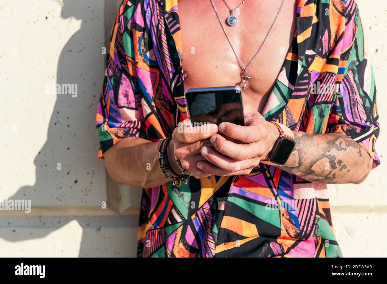 Crop view of hipster man leaning on wall chatting on social media via mobile phone on sunny day Stock Photo