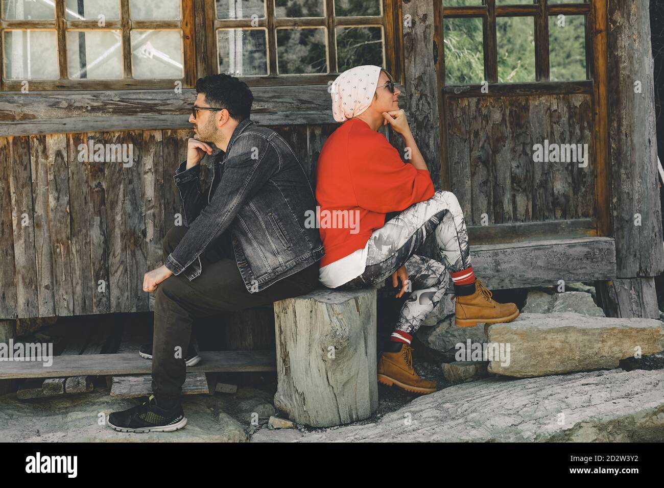 Couple sitting back to back in front of the house Two sulky adults turned away from each other. Stock Photo