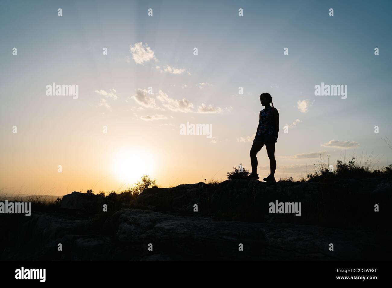 Side view silhouette of unrecognizable female hiker standing on top of hill and admiring landscape of highlands at sunset time Stock Photo