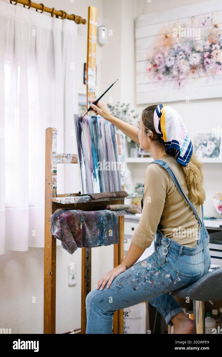 Side view of female artist sitting near easel and drawing colorful ...