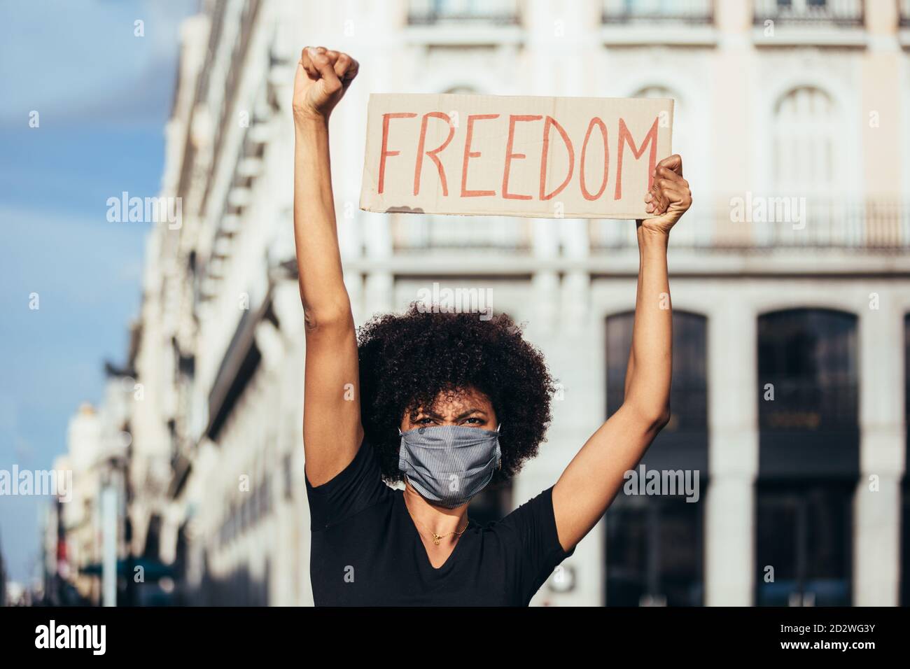 Afro Woman protesting at a rally for racial equality. She is raising fist holding a sign with the word "Freedom". Black Lives Matter. Stock Photo