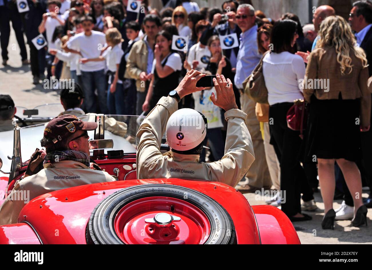 SAN MARINO, SAN MARINO - MAY 13, 2011: A BMW 328 during the Mille Miglia 2011 in San Marino, people waving BMW flags, copilot taking photographs. Stock Photo