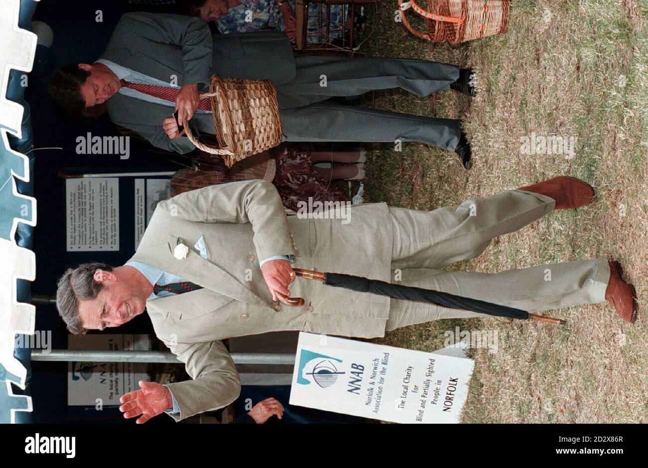 The Prince of Wales waves to well wishers, while his Royal protection officer (right) is left to pick up the bill for a wicker basket that the Prince purchased at the Sandringham show this morning (Wednesday). PHOTOGRAPH BY JOHN STILLWELL/PA. Stock Photo