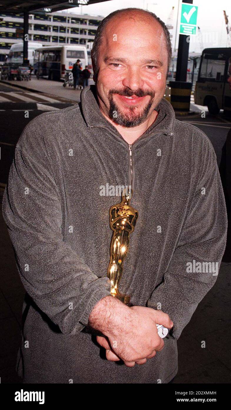 British director Anthony Minghella proudly clutches his Oscar on arrival at Heathrow Airport.  It is his first return to Britain since his film, 'The English Patient' won nine Oscars at last week's awards ceremony in Hollywood. Stock Photo