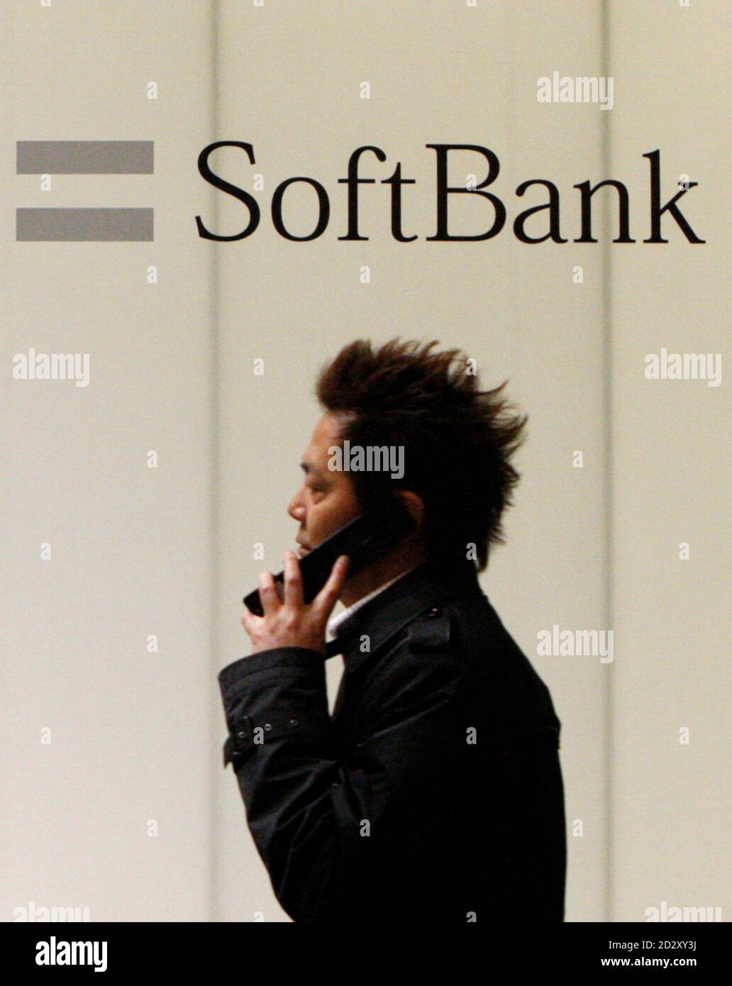 A man using a mobile phone walks past an advertisement board of Softbank Corp in Tokyo February 5, 2009. Softbank Corp, Japan's No.3 mobile phone operator, posted a 2.4 percent rise in quarterly profit as a drop in cellphone sales lowered its subsidy payments, and it stuck to its full-year forecast. REUTERS/Toru Hanai (JAPAN) Stock Photo