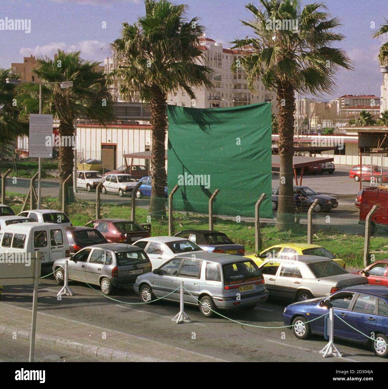 A massive curtain hangs from two palm trees as cars queue to cross the Gibraltar border.  The curtain has been erected by the Spanish authorities to block the view of Gibraltar-based Internet camera showing the queues of traffic on a web site.  PA photo: Gibraltar Chronicle. Stock Photo