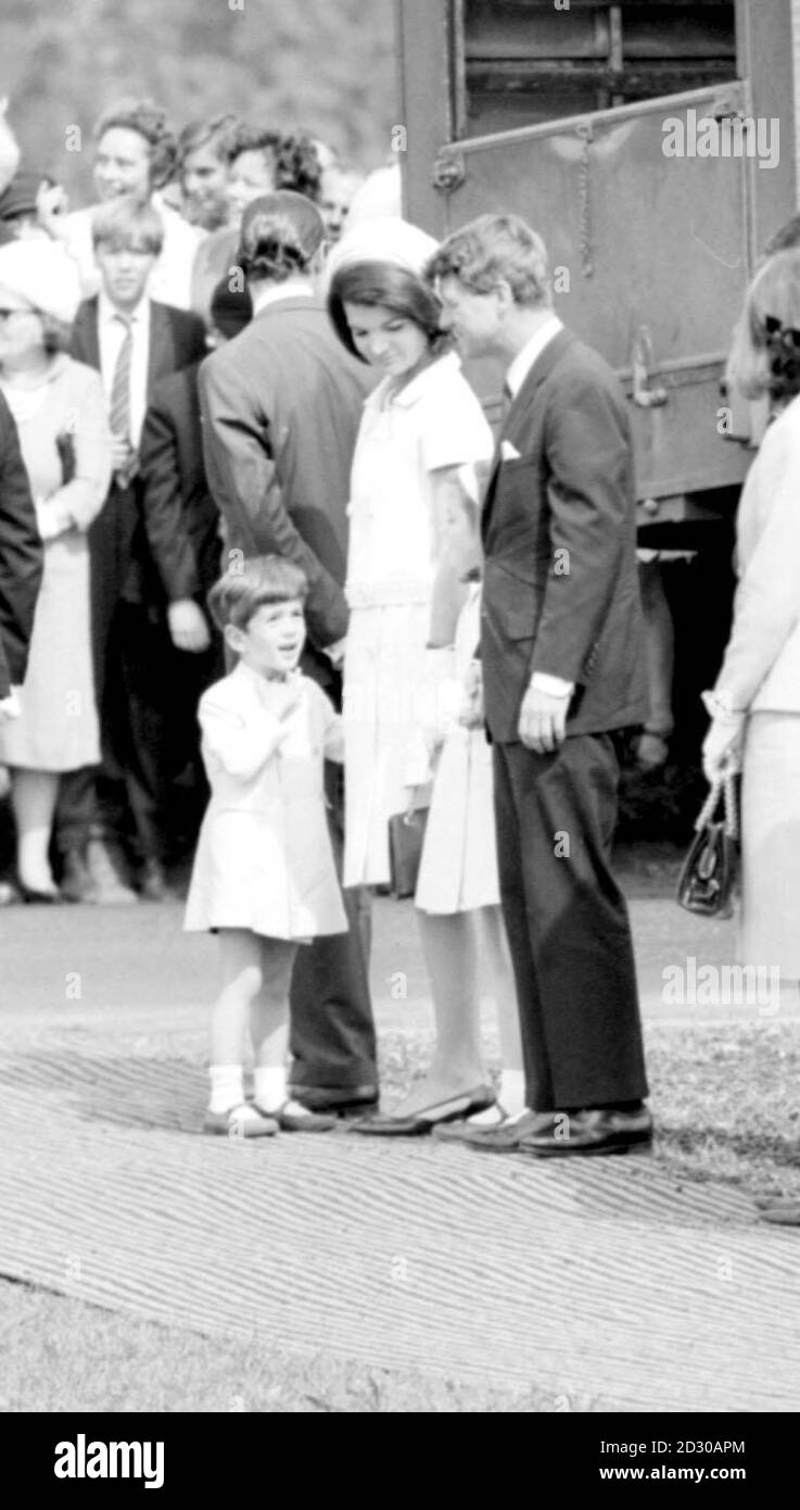 John fingers his collar as he talks with his uncle, Senator Robert Kennedy, while waiting with his mother, Jacqueline Kennedy, and sister Caroline to meet the Queen at the Kennedy Memorial site, in the meadows of Runnymede beside the Thames. Stock Photo