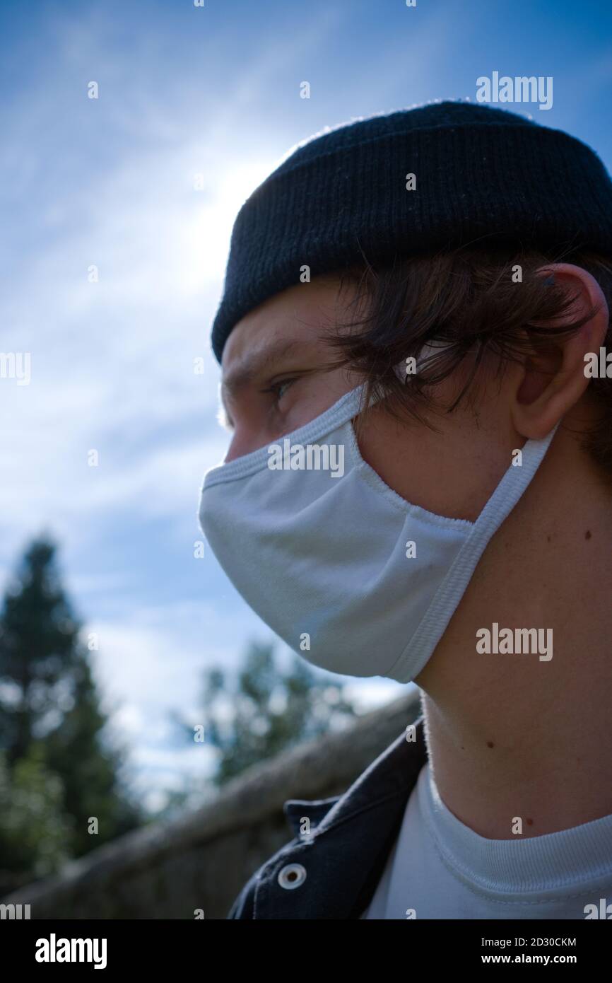 facial profile of an eighteen year old man with a hat and wearing a white cotton reusable anti viral face mask outside in scotland Stock Photo