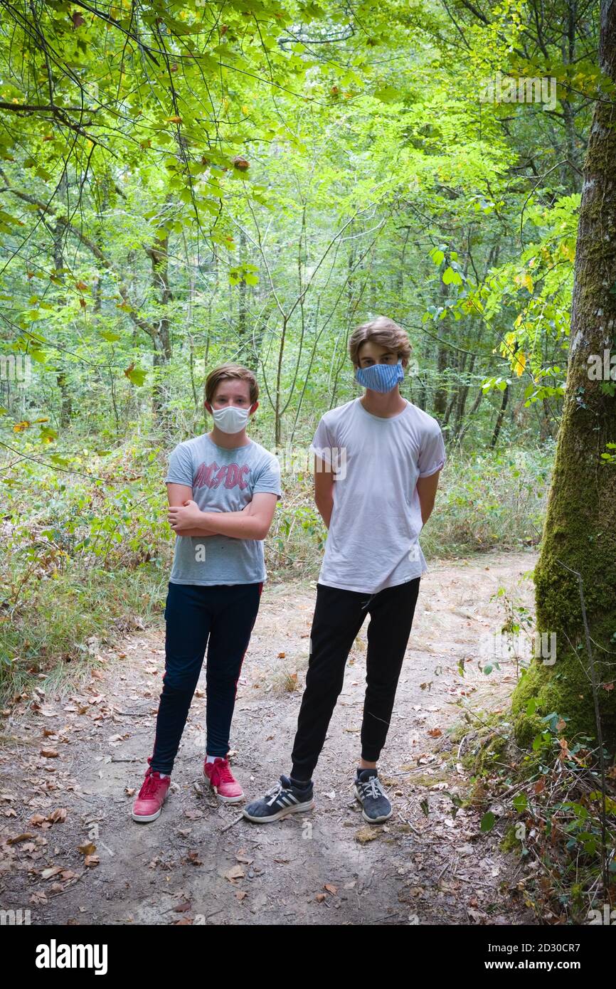 portrait of two male teenagers wearing face masks against covid stand together on a path in a forest on a summer days walk Stock Photo