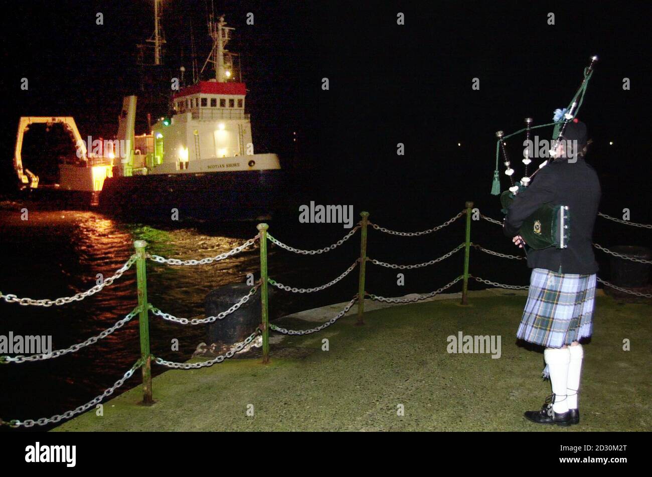 A lone piper sees in the Scotian Shore boat carrying the bodies of the seven victims of the Solway Harvester on the quayside in Douglas, Isle of Man. Stock Photo