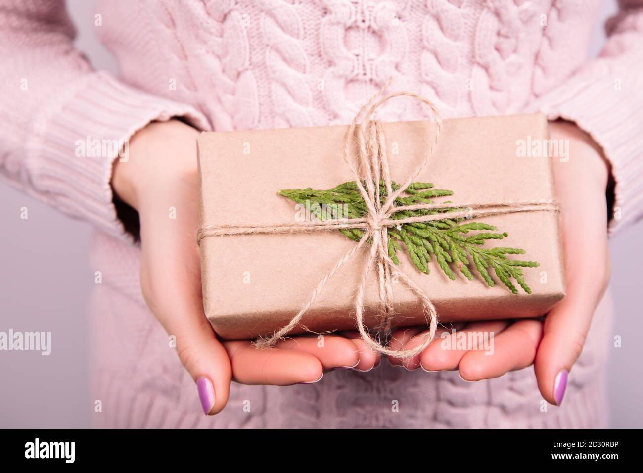 Woman's hands in pink jumper holding craft paper gift box with a present for Christmas, new year, valentine day or anniversary on black background, to Stock Photo