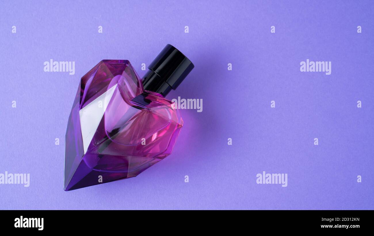 Isolated heart shaped perfume bottle on purple background. Gift concept. Fragrance spray mock up. Romantic scent Stock Photo