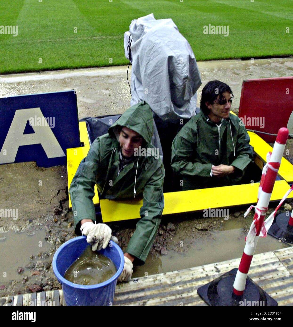 A television crew use a bucket to empty their camera pit of rain water as they prepare to cover the World Cup qualifier football match between England and Germany at London's Wembley Stadium. Stock Photo