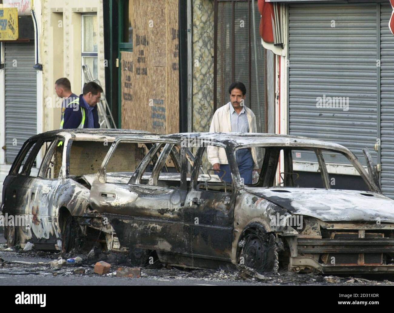 Cars lie burned out while shop windows are boarded up after being smashed  in a night of riots in Burnley, Lancashire. A newsagent's shop, pub, sex  shop and at least five cars