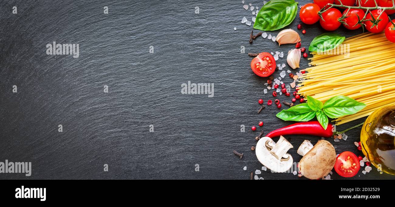 Food ingredients on dark background. Tomatoes, spaghetti, spices, garlic and basil leaves on black background. Italian food, health or cooking concept Stock Photo