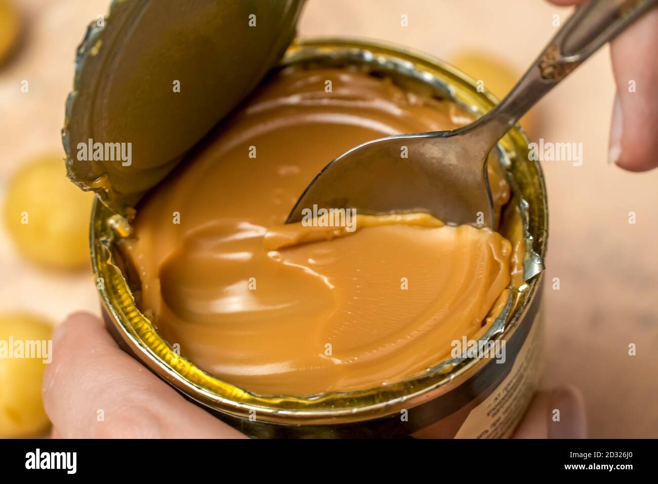 woman's hand takes a teaspoon of boiled condensed milk from a tin can