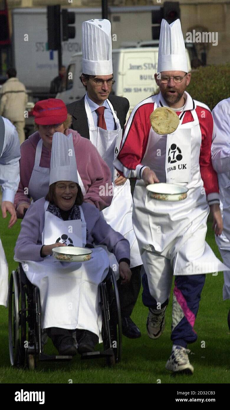 Ann Begg, MP for Aberdeen Southand (in wheelchair) and Tony Cunningham MP for Workington (right) take part in the annual Shrove Tuesday Parliamentary pancake race on the green opposite the House of Lords in Westminster, London.   * The event, in aid of brain injury charity Rehab UK, involves a team of MPs and a team from the Lords donning tall chefs' hats and whites and racing each other while tossing pancakes three feet into the air. Stock Photo