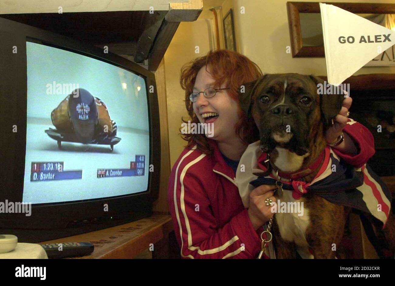 Alex Coomber's proud 12 month old boxer 'Foggy' with friend Alce Harfield and the tv at Dean, Somerset showing Alex gaining a bronze medal in the Winter Olympics.  Stock Photo