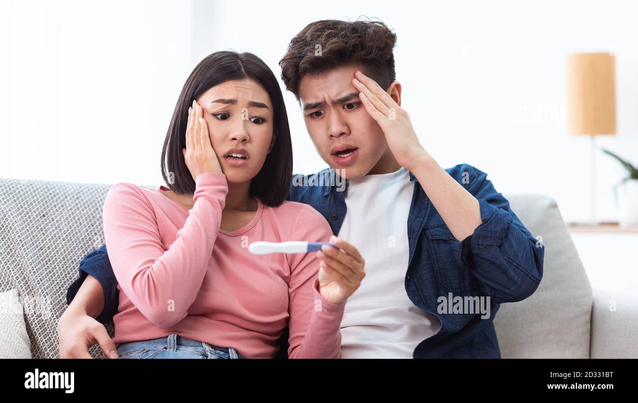 Unhappy Young Asian Couple Holding Positive Pregnancy Test Indoor, Panorama Stock Photo