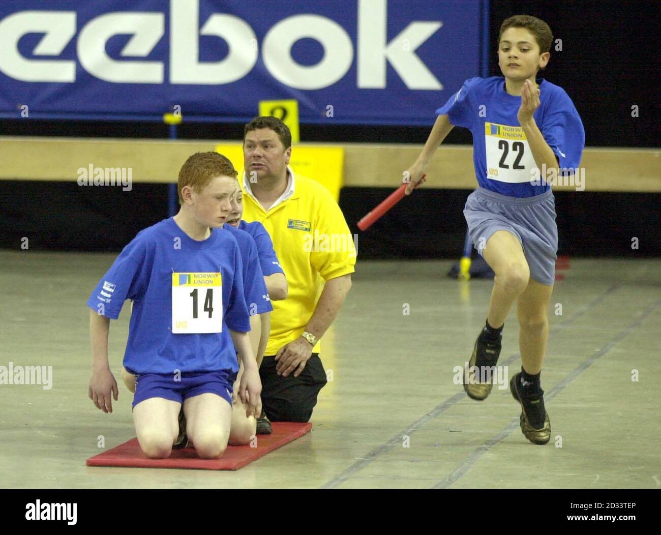 Ellis Harding (No 22) from Nottinghamshire (Under-13 boys) in action during the 4x2 Relay, watched by team-mate Richard Barnes (No 14) during the UK National Final for Young Athletes at the National Indoor Arena, Birmingham. Forty-eight teams from all over the country contested in the final. Stock Photo
