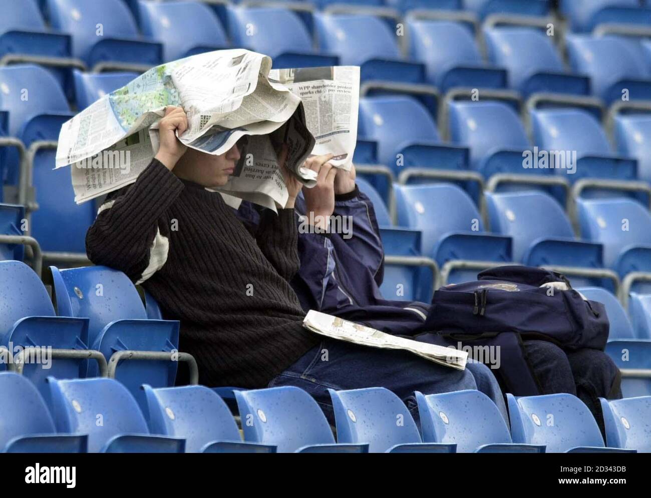Two cricket fans wait patiently under cover for play to start between England against Zimbabwe after rain delayed the NatWest Series match at Headingley, Leeds. Stock Photo