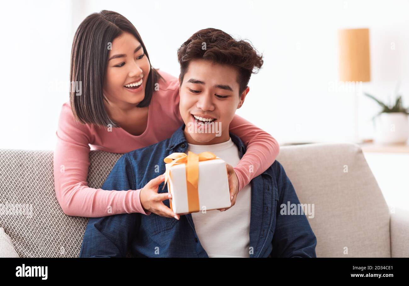 Chinese Girlfriend Giving Gift Box To Surprised Boyfriend At Home Stock Photo