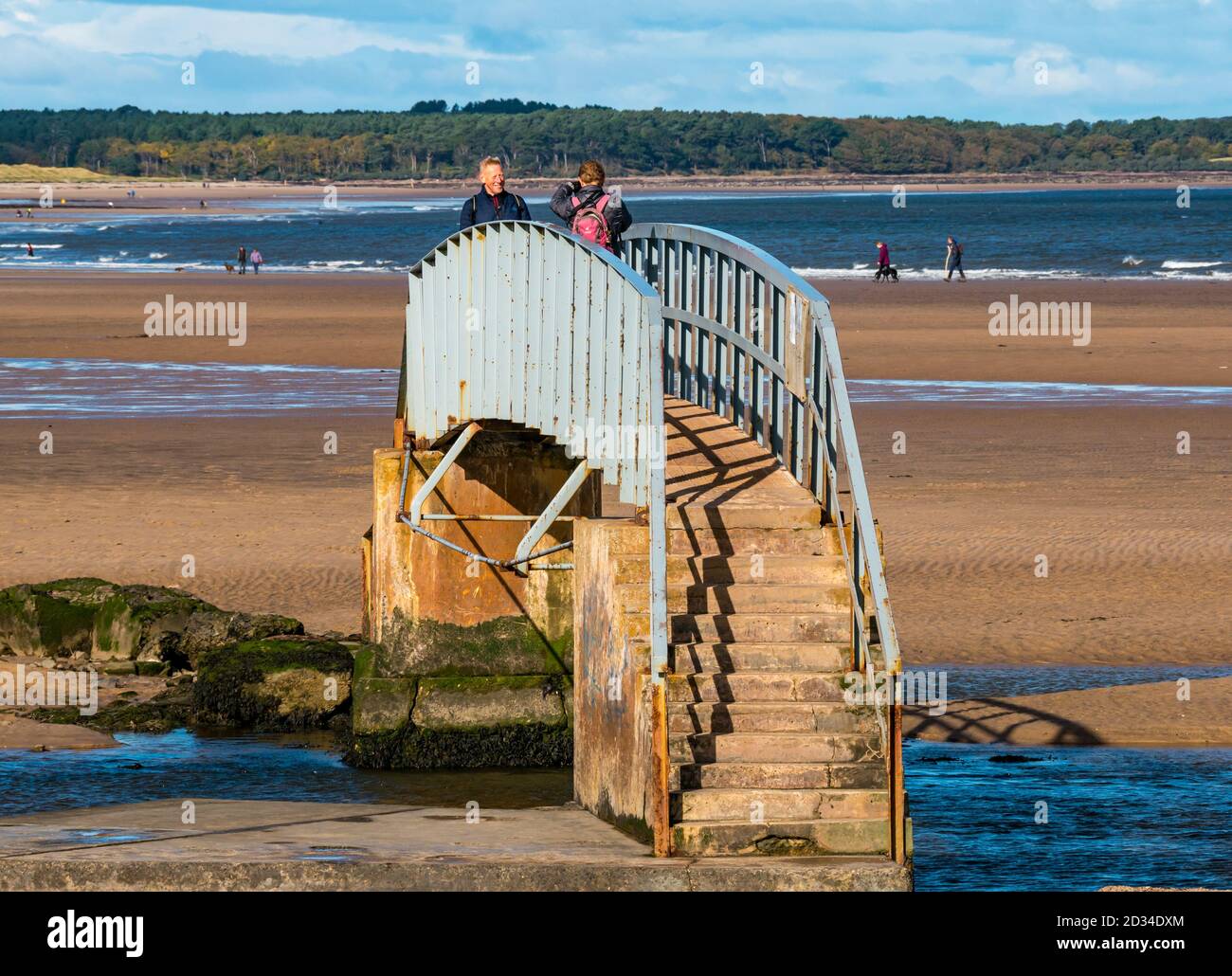Belhaven, East Lothian, Scotland, United Kingdom, 7th October 2020. UK Weather: sunshine on the Bridge to Nowhere. The bridge over the Biel Water is only accessible at low tide for visitors to the beach at Belhaven Bay. A couple walk over the unusual bridge Stock Photo