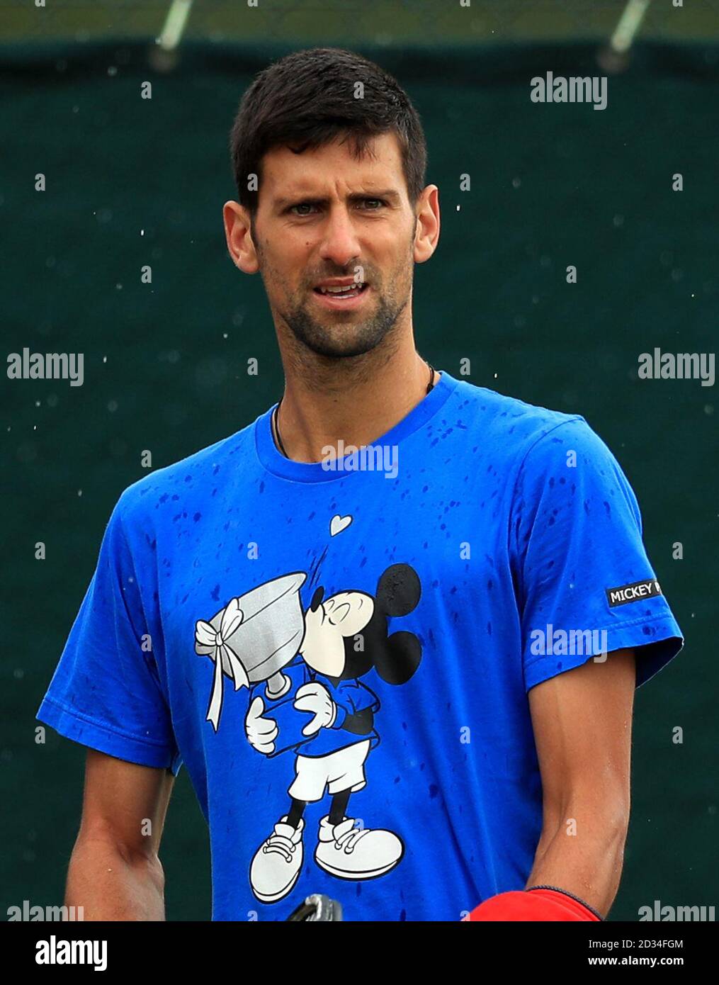 Novak Djokovic sports a Mickey Mouse kissing a trophy t-shirt ahead of a practice session on day Three of the Wimbledon Championships at the All England Lawn Tennis and Croquet Club, Wimbledon. Stock Photo