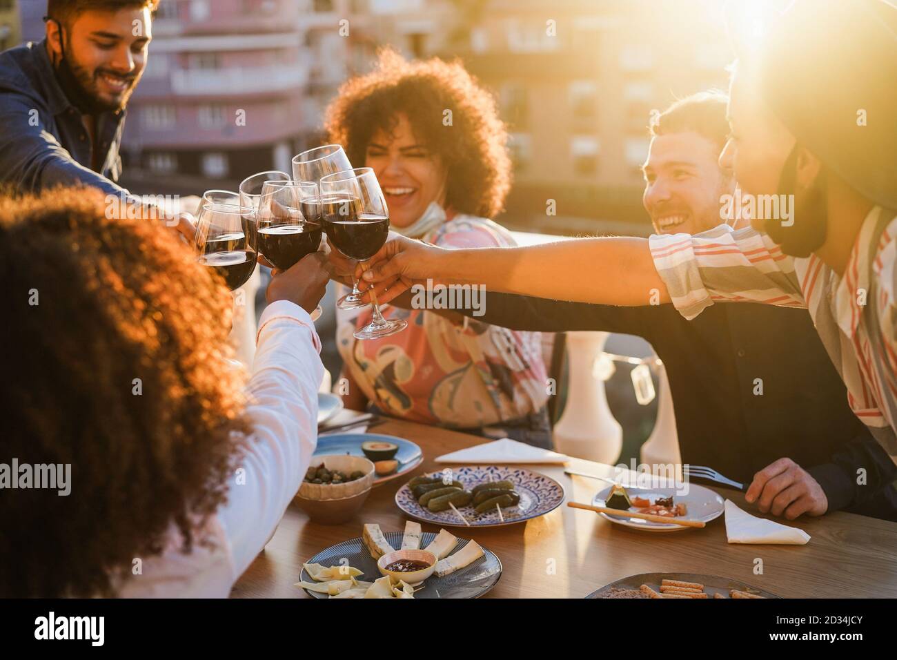 Young multiracial people cheering with wine at party dinner while wearing protective masks - Social distance concept - Focus on hands glasses Stock Photo