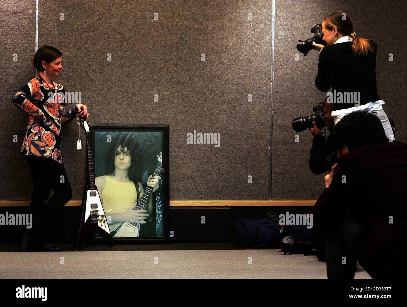 A Christie's member of staff holds a Gibson Flying V guitar owned by T-Rex guitarist Marc Bolan as it stands next to his portrait at the auctioneers in London's Old Brompton Road. Stock Photo