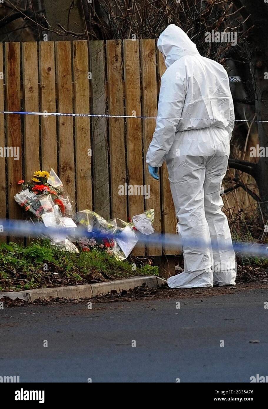 A Police forensic officer looks at floral tributes at the house in Wakefield where Archie-Lee Hirst was killed by a dog. Stock Photo