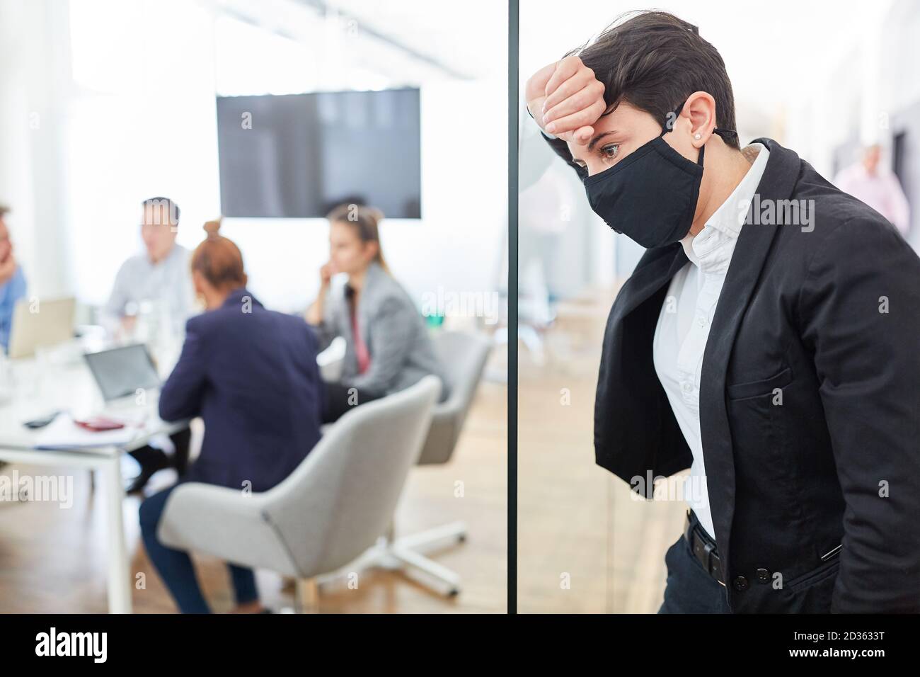 Exhausted business woman with everyday mask leans tiredly against a glass wall Stock Photo