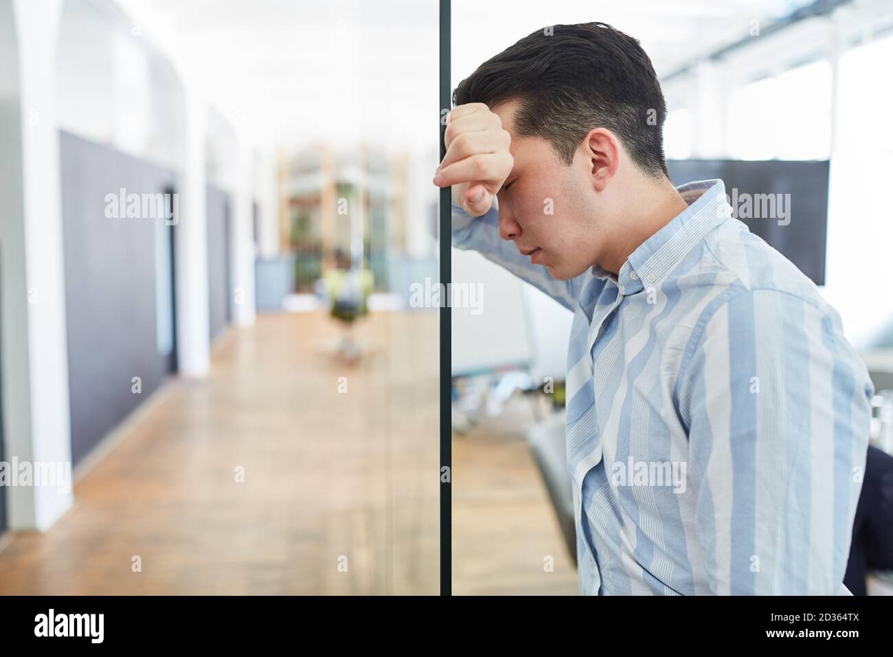 Young business man in office with burnout due to overload leaning against glass wall Stock Photo