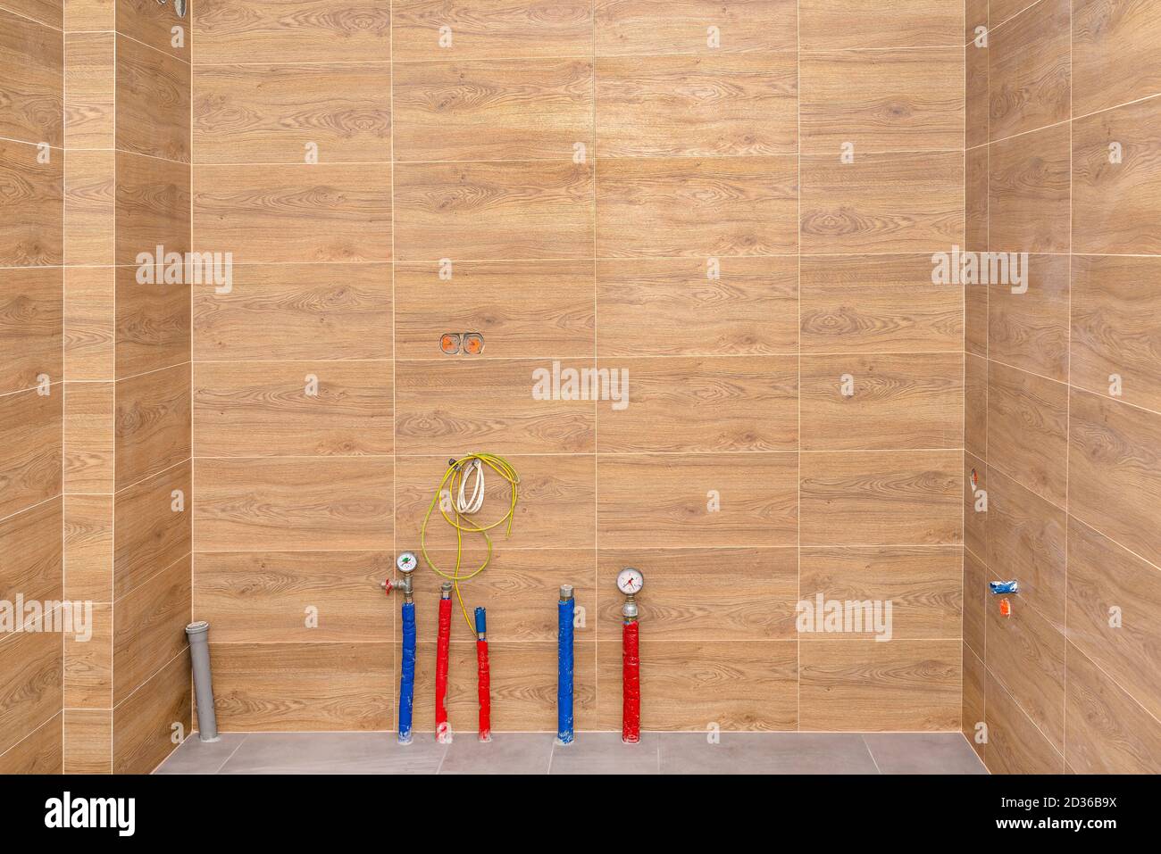 Water pipes, underfloor heating pipes and sewage system coming out of the floor in a modern boiler room made of brown ceramic tiles. Stock Photo