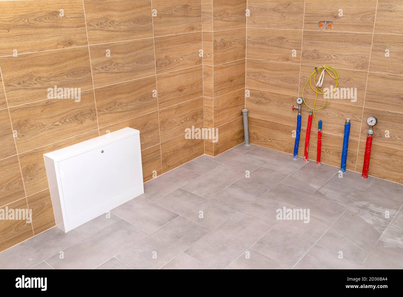 Water pipes, underfloor heating pipes and sewage system coming out of the floor in a modern boiler room made of brown ceramic tiles. Stock Photo