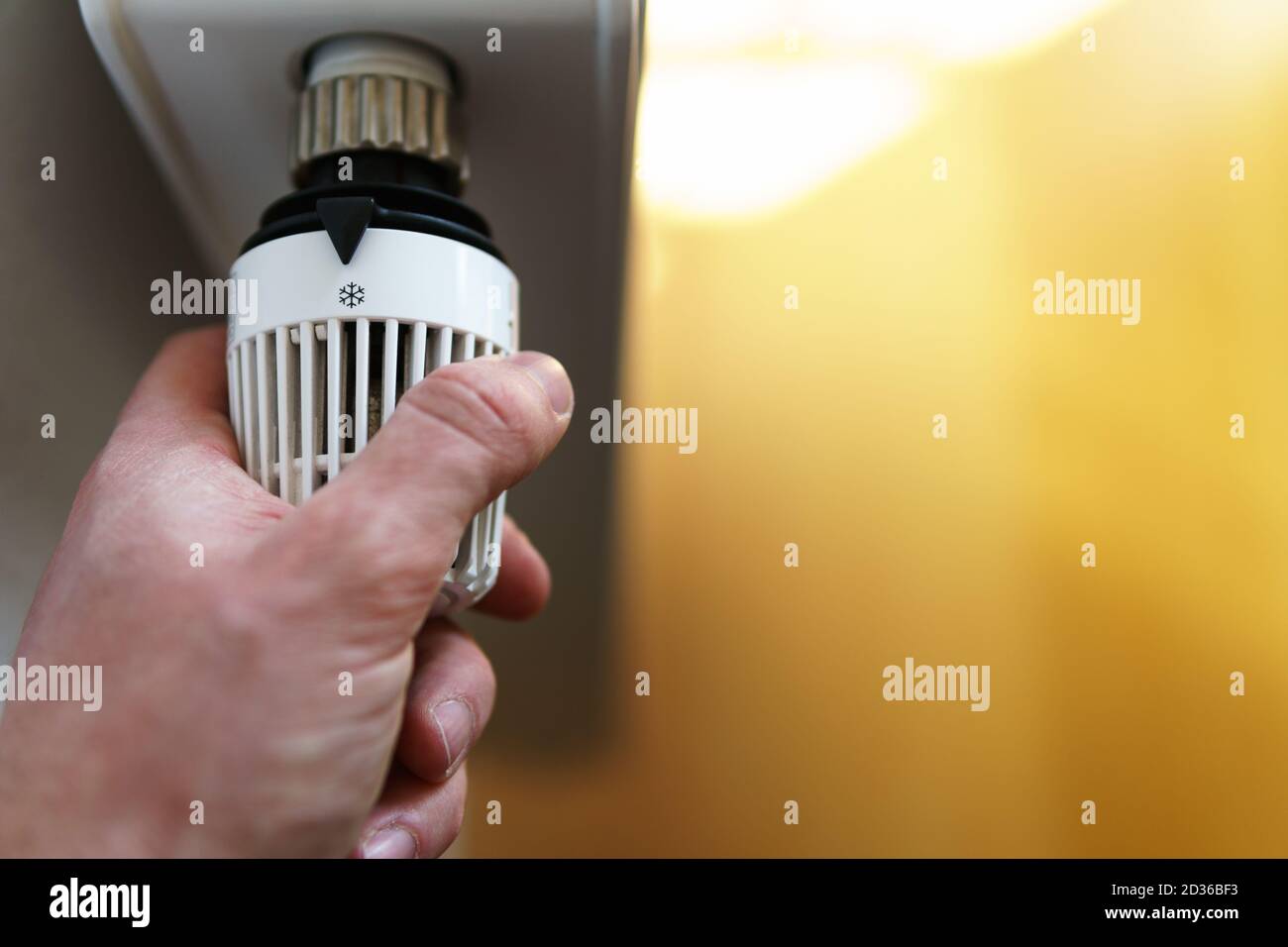 Hand of man adjusting radiator thermostat valve to snow flake frost icon, symbol for saving money at heating costs or low temperature, closeup. Stock Photo