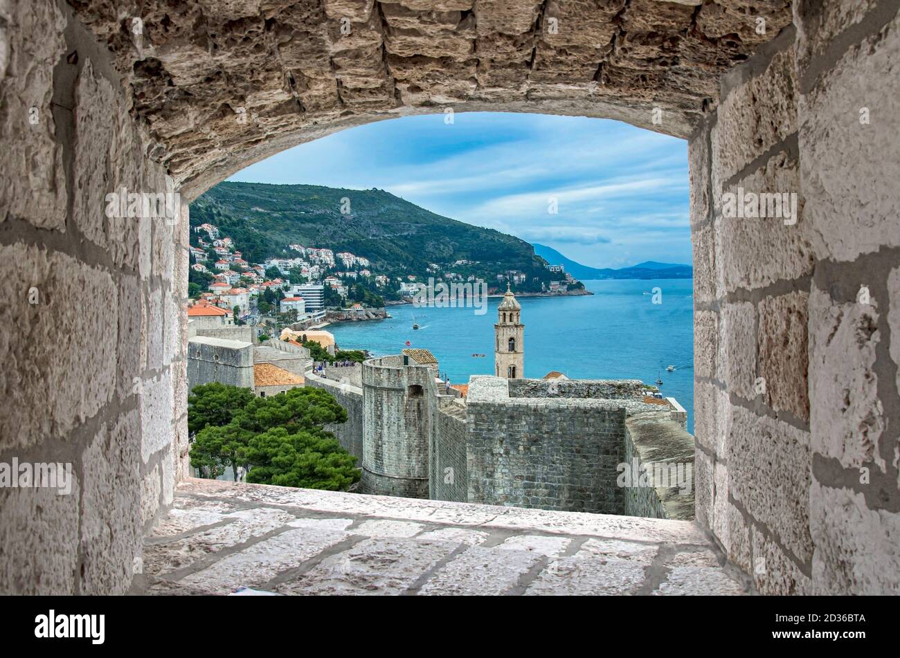 View of Dubrovnik wall, tower and blue sea during sunny summer day from stone window in Dubrovnik, Croatia. Stunning view of Dubrovnik city walls and Stock Photo