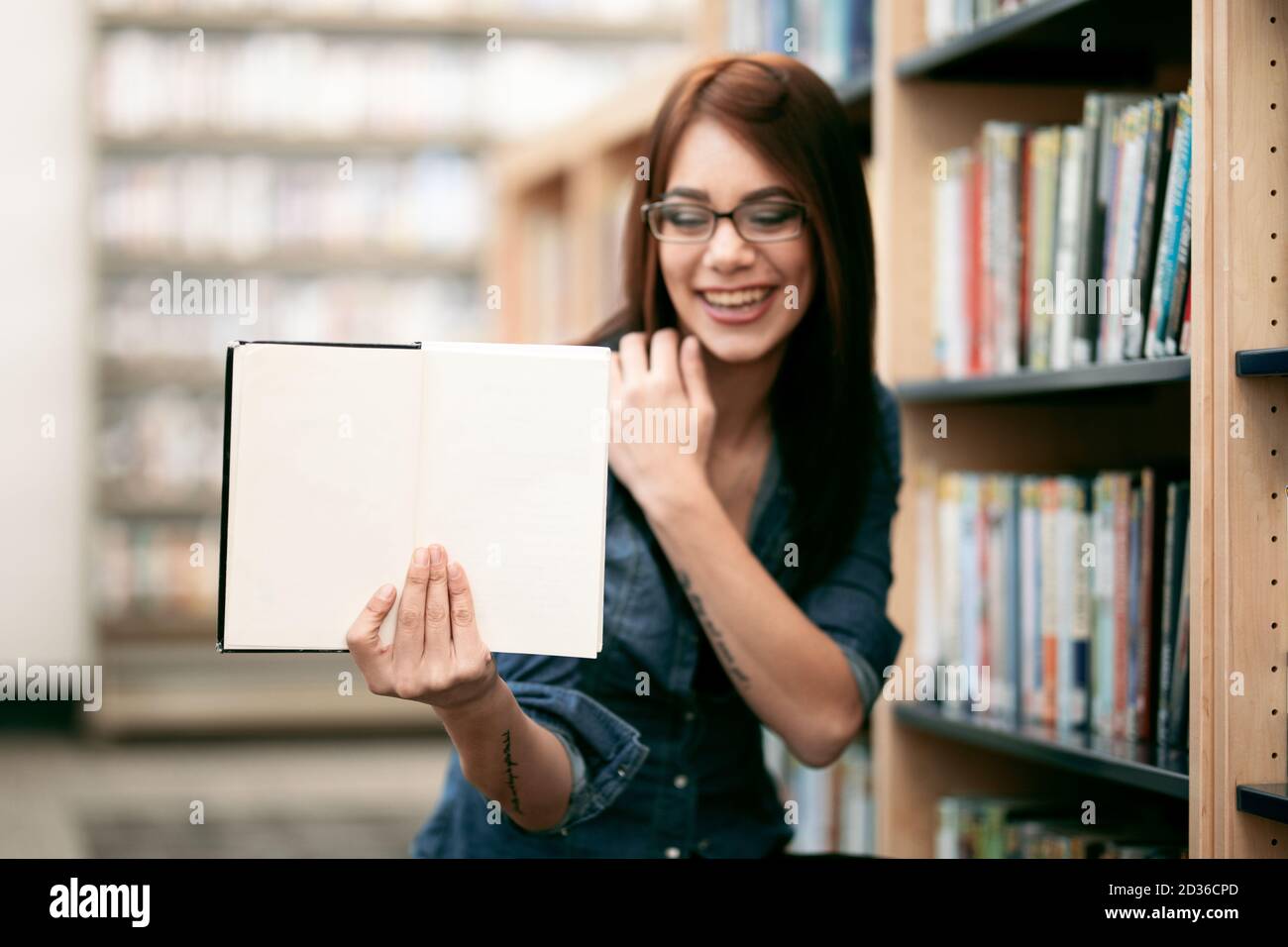 A solitary young woman holding a book with blank copy space at her local library with view of book shelves and bookcases. Stock Photo
