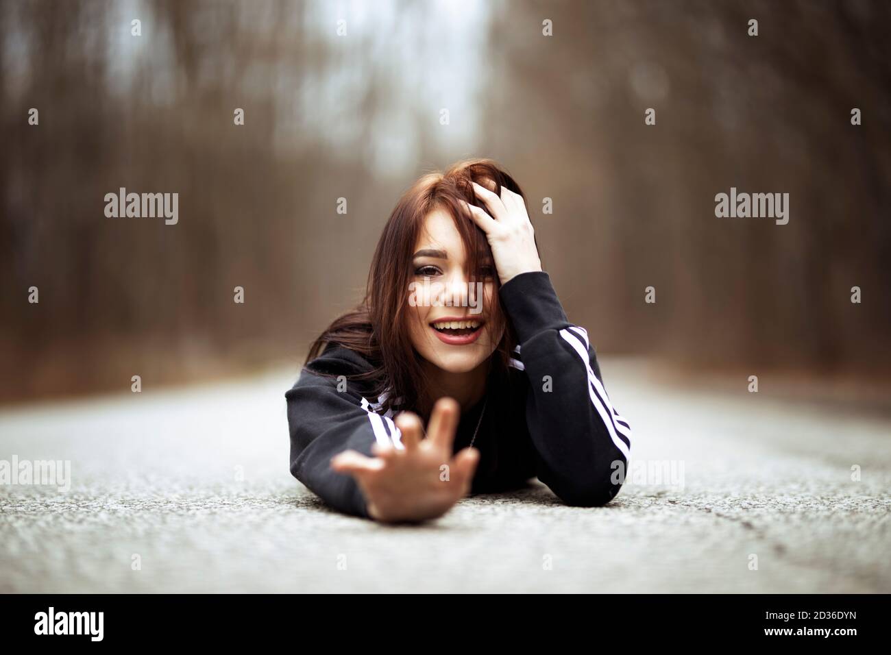 A solitary young poses on the ground in the middle of a road, reaching out with a smile Stock Photo